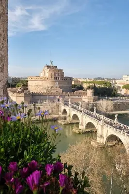 a bridge over a river in a city with purple flowers at La Torre di Castel Sant'Angelo in Rome