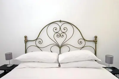 a white bed with a metal headboard with white pillows at Cozy Merulana in Rome