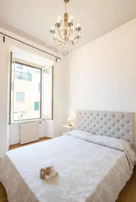 a white bedroom with a large bed and a chandelier at ROMA your home in trastevere e gianicolo in Rome