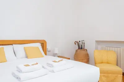 a bedroom with a white bed with a yellow chair at St Peters Garden 3 BDR Apartment in Rome