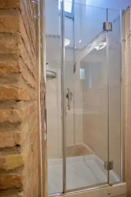 a glass shower in a bathroom next to a brick wall at Fororomano Luxury in Rome