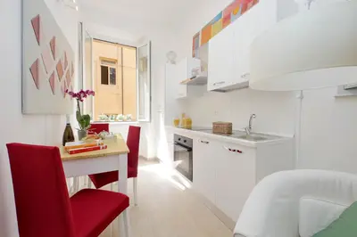 a white kitchen with a table and red chairs at NuvolHouse in Rome
