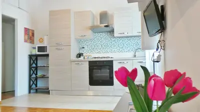 a kitchen with white cabinets and pink flowers at Casa Tua a Monti in Rome