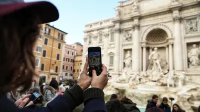 a woman taking a picture of a fountain with her cell phone at 47LuxurySuites - Trevi in Rome