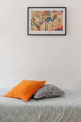 an orange pillow on a bed with a picture on the wall at central little basic apartment in Rome