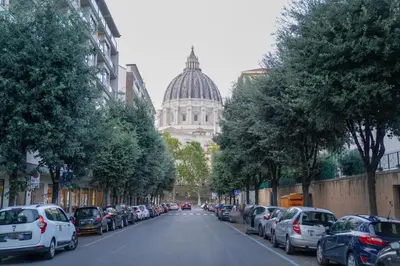 a street with cars parked on the side of a street with a cathedral at San Peter loft in Rome