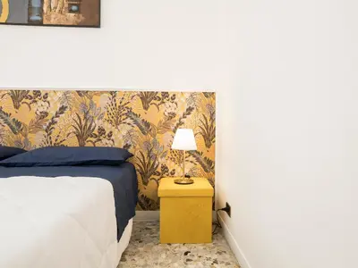 a bedroom with a bed and a yellow table with a lamp at Blessy apartment Vaticano in Rome