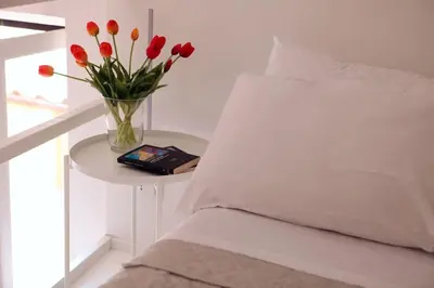 a vase of red flowers on a table next to a bed at Scarpetta32 - Your home in Trastevere in Rome