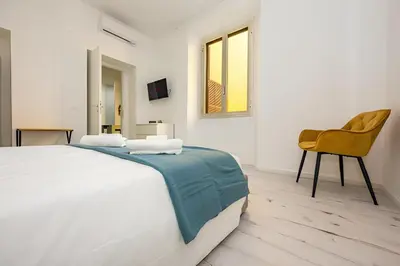 a white bedroom with a bed and a yellow chair at 1 Minute from San Pietro - Nicole House in Rome