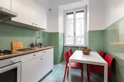 a kitchen with green and white walls and a table with red chairs at Angelico Vatican Apartment by Oneup Hospitality in Rome