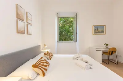 a white bedroom with a bed and a desk and a window at Faleria by Rental in Rome in Rome
