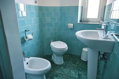 a blue tiled bathroom with a toilet and a sink at Carolina Trastevere House in Rome