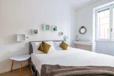 a white bedroom with a large bed and a stool at Urban Chic 2 BR Vatican Escape in Rome