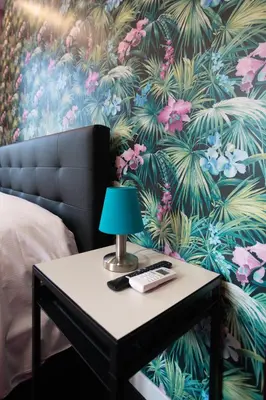 a nightstand with a lamp on a table with a tropical wallpaper at SABA SUITE ROMA in Rome