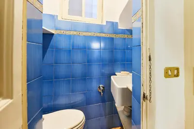 a blue tiled bathroom with a toilet and a window at iFlat Magnificent flat near the Colosseum in Rome