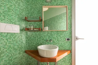 a green tiled bathroom with a sink and a mirror at Casa Angelica, a Burghesius home in Rome