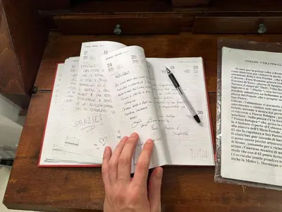 a person is writing on a book with a pen at Profumo di Sorrento a Roma in Rome