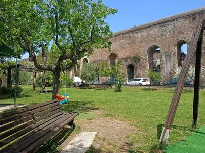 a park bench in front of a large brick building at TWO-ROOM Apt. under the Aqueduct's ARCH in Pigneto in Rome