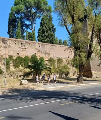 a group of people walking down a street next to a wall at The Golden Pyramid in Rome