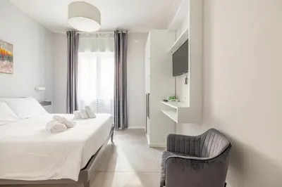 a white bedroom with a bed and a chair at Belli Suites Vatican Rome Guest House in Rome