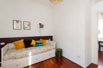 a white bedroom with a bed with colorful pillows at Mecenate Suite Colosseum in Rome