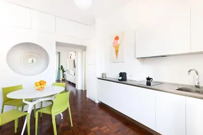 a white kitchen with a table and green chairs at Idyllia - Bright and modern apt in Rome