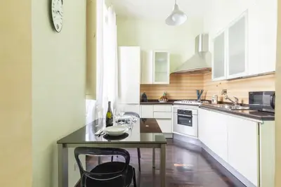 a kitchen with white cabinets and a table with a clock at Hostly-Urban Oasis Turati-Few Steps from Colosseum in Rome