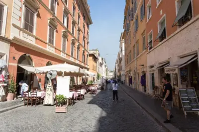 a man walking down a street with tables and chairs at San Peter Borgo 68 in Rome