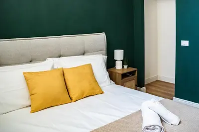 a white bed with yellow pillows and a green wall at Domina Apartments Roma - San Pietro 2 in Rome