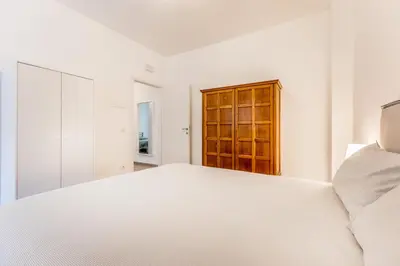 a white bedroom with a white bed and a wooden cabinet at Al 32C del Gianicolo in Rome