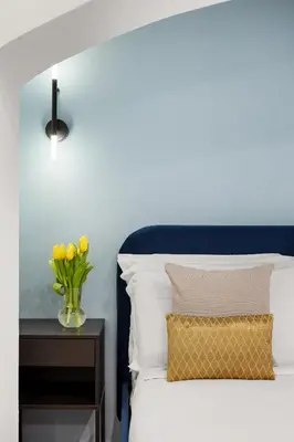 a bed with a blue headboard and a vase of yellow tulips on at Leopardo Boutique Apartment in Trastevere in Rome