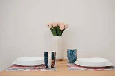 a table with plates and a vase with pink flowers at 20 Minuti Vaticano - Nido Romano Shopping Folkoristico by Hôtea in Rome