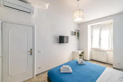 a white bedroom with a blue bed and a window at DOMVS Quattro Venti in Rome