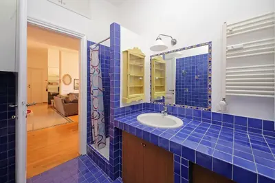a blue tiled bathroom with a sink and a mirror at Parioli, Bright And Quiet 2BR Apartment By Halldis in Rome