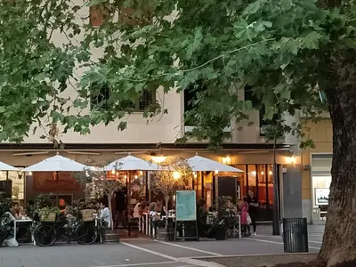 a restaurant with tables and umbrellas in front of a building at A bridge to the Coliseum in Rome