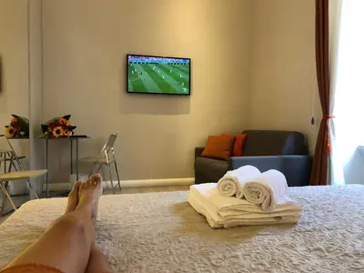 a person with their feet up on a bed watching television at The Roman Empire Guesthouse in Rome