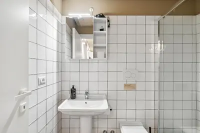 a white tiled bathroom with a sink and a toilet at Limehome Rome Via Fortebraccio in Rome