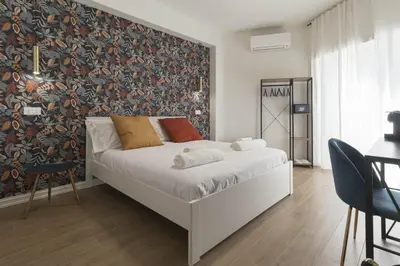 a bedroom with a white bed with a wall with a floral wallpaper at GENESI Suites in Rome