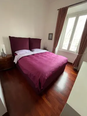 a bedroom with a bed with a purple comforter and two windows at Casa Ale in Rome