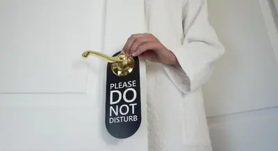 a person in a white robe unlocking a door with a do not disturb tag at NEXUS Palace in Rome