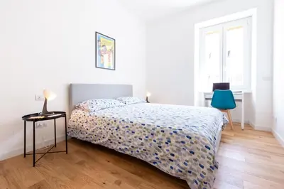 a white bedroom with a bed and a blue chair at L'Appartamentino a San Giovanni in Rome