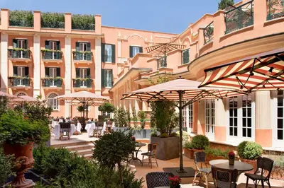 a patio with tables and umbrellas in front of a building at Rocco Forte Hotel De La Ville in Rome