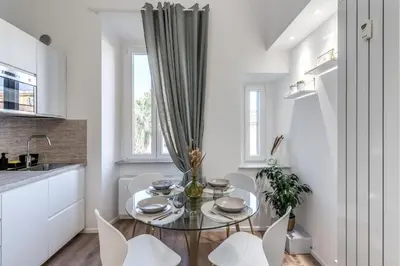 a white kitchen with a glass table and white chairs at St Peter Miracle Suite in Rome