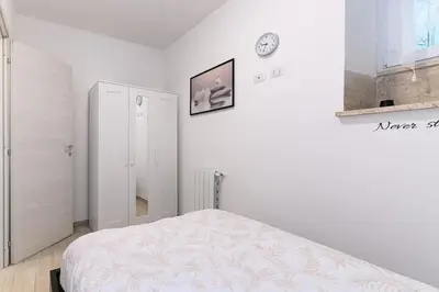 a white bedroom with a bed and a clock on the wall at La Scaletta Furio Camillo in Rome