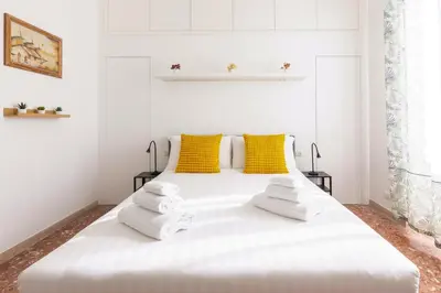 a white bed in a white room with yellow pillows at Hostly-Maison Sant'Angelo-Few steps from Vatican in Rome