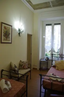 a room with two beds and a chair and windows at Tucci's Roma Guest House in Rome