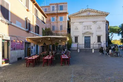 a group of tables and chairs under an umbrella on a street at Rome As You Feel - Designer two-level apartment in the heart of Trastevere in Rome
