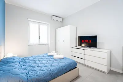 a white bedroom with a blue bed and a tv at MagicHouse 2 Camere 2 Bagni -15 min Colosseo in Rome