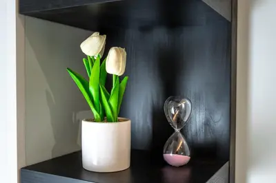 a black shelf with a clock and a vase with flowers at Suite Room Suriani in Rome