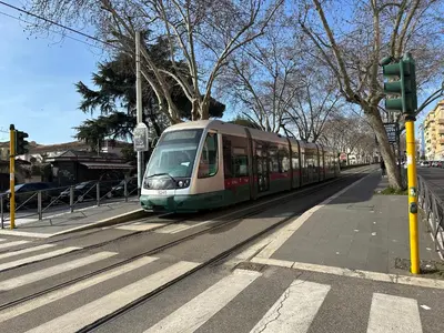 a train is traveling down the tracks on a street at Relais Trastevere Station in Rome